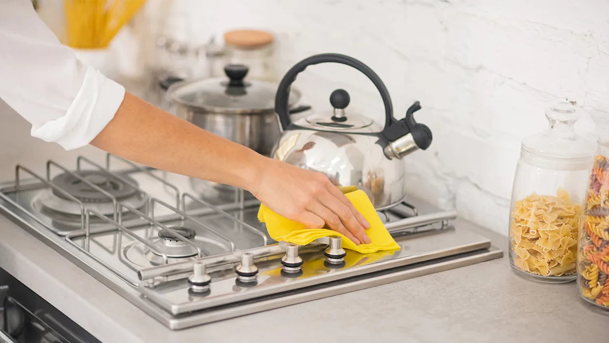Person cleaning a stovetop with a yellow cloth in a kitchen.