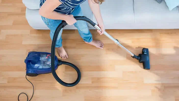 Person using a vacuum cleaner on a wooden floor