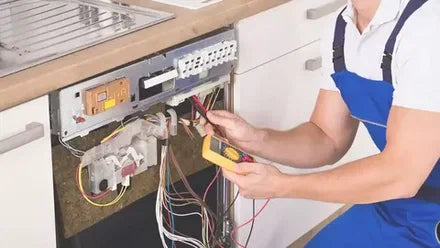 Person repairing a dishwasher with a multimeter in a kitchen setting