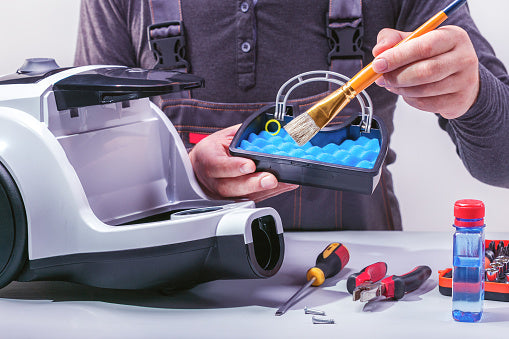 Person cleaning a robot vacuum cleaner with tools on a table