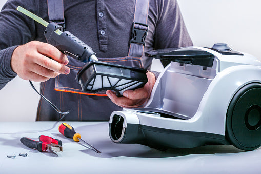 Person repairing a vacuum cleaner with tools on a white surface