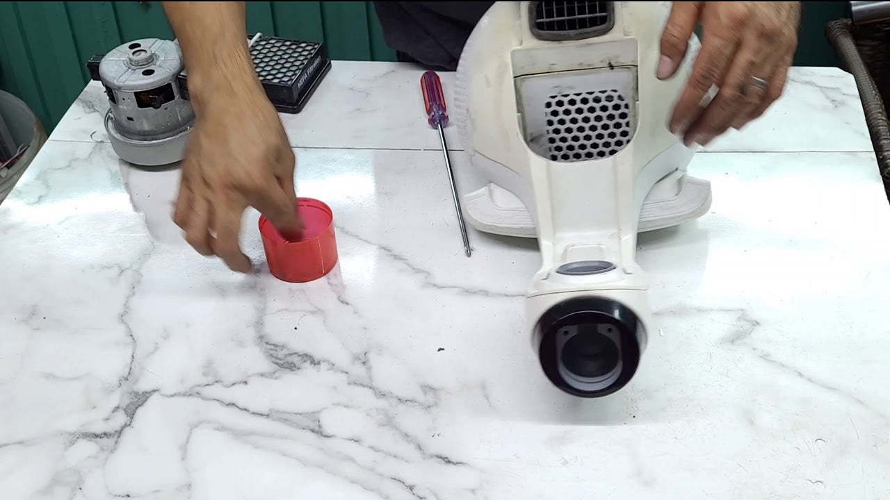 Person cleaning a white appliance with a red sponge on a marble surface